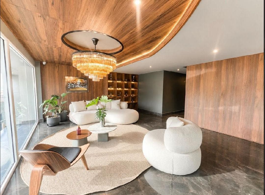 Salón lujoso con techo de madera curvo, gran candelabro, sofás blancos redondeados y alfombra circular.