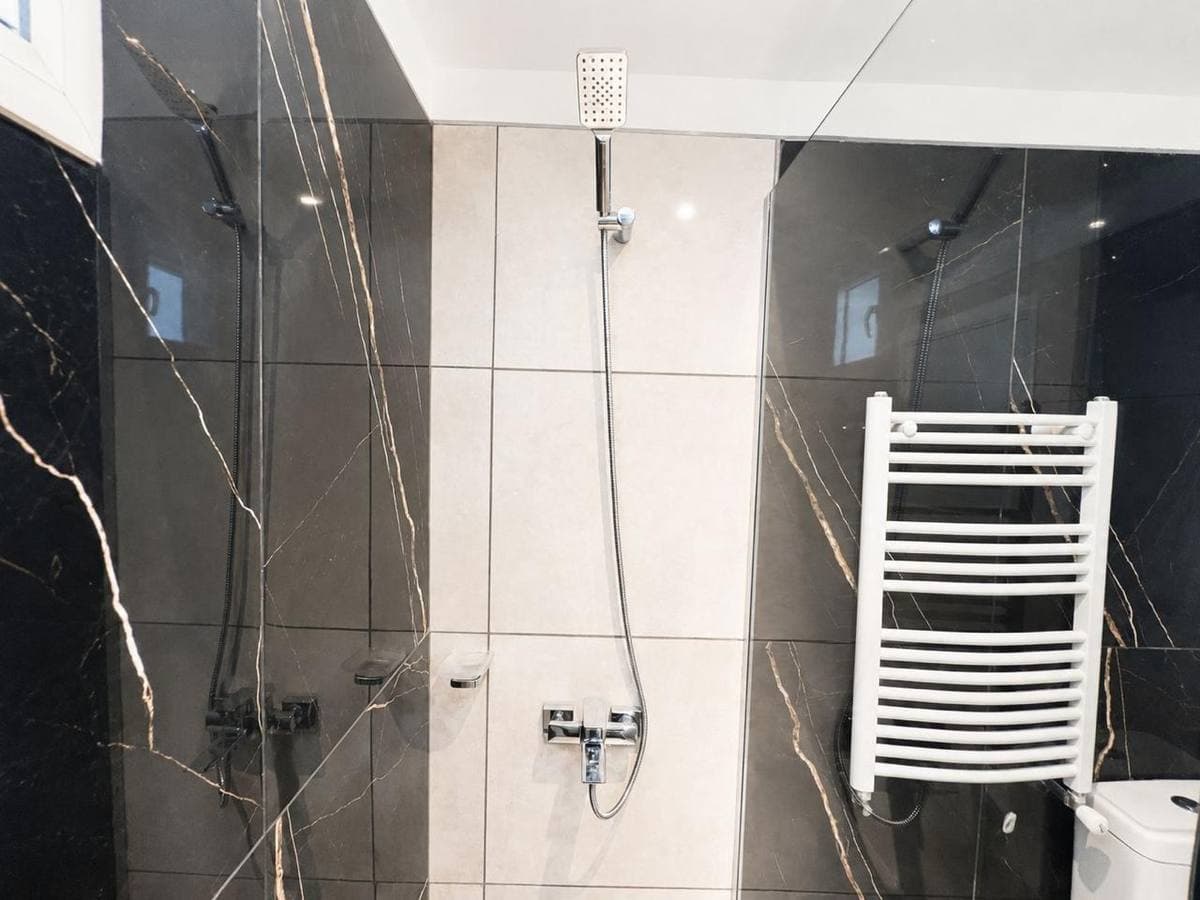 Ducha moderna con azulejos de mármol negro y blanco, grifería cromada y toallero blanco.