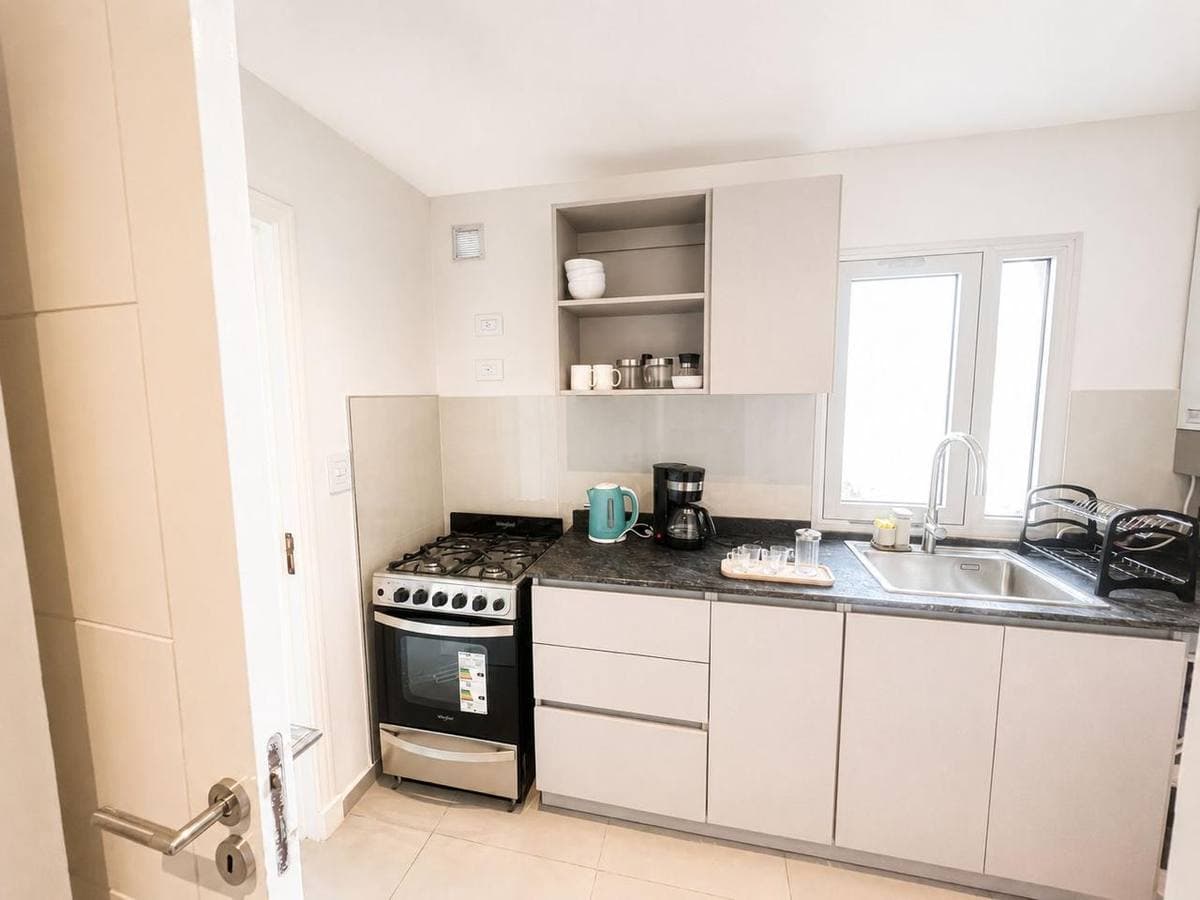 Cocina moderna con armarios blancos, encimera gris, estufa negra y fregadero bajo la ventana.