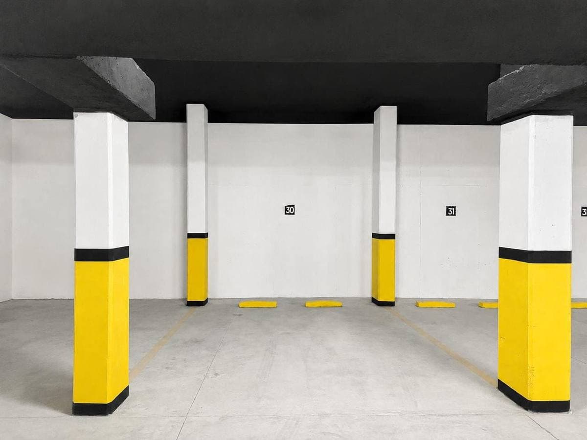 Garaje vacío con columnas amarillas y blancas, techo negro y espacios de estacionamiento numerados.